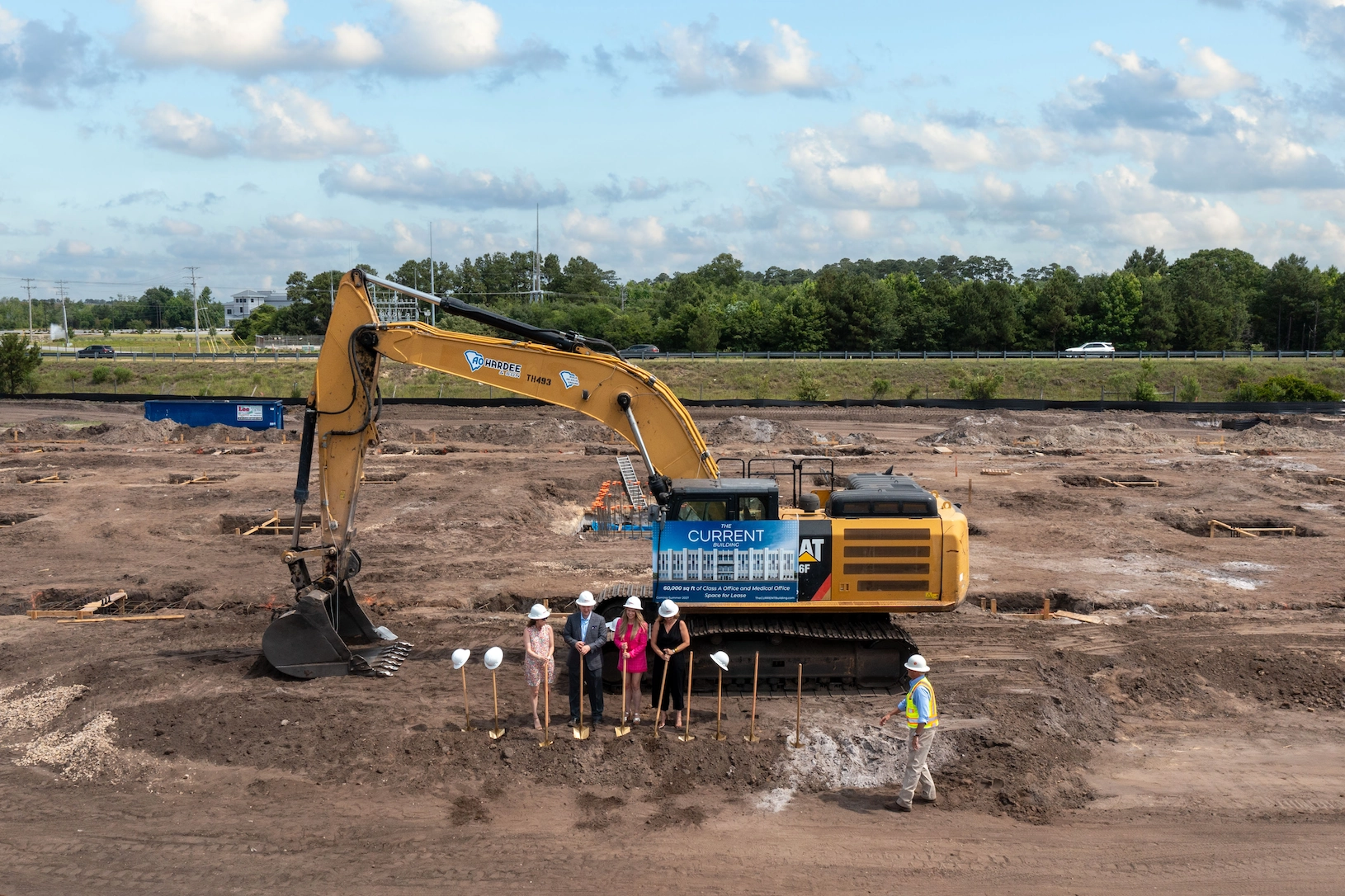 Official groundbreaking with excavator and principals holding ceremonial shovels